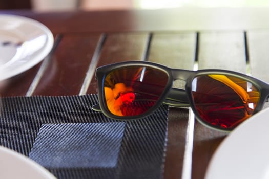 A man is reflected on a colorful sunglasses during his breakfast on vacations. The table has a tablemat and white plates.