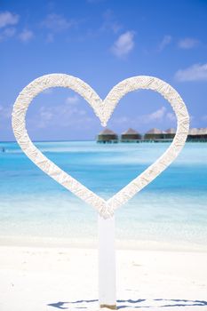 Heart to shoot photos of honeymoon couples in the beach in Maldives with a tropical background with bungalows over water. It is a beautiful sunny day with few clouds.