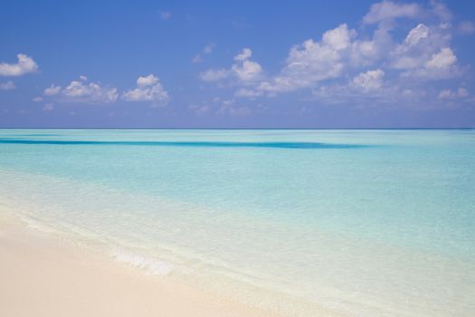 Tropical beach in paradise with clear crystal water in Maldives. Beautiful tones of turquoise in the sea. The sky is partial covered with clouds.