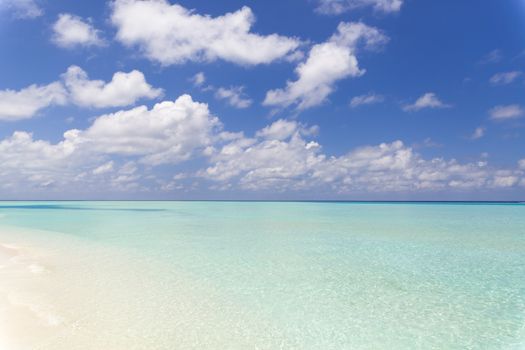 Tropical beach in paradise with clear crystal water in Maldives. Beautiful tones of turquoise in the sea. The sky is partial covered with clouds.