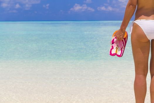 Woman holding flip flops while standing on the beach.