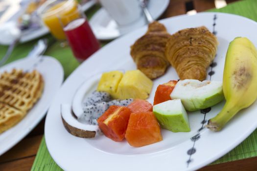 Delicious healthy breaklfast outdoors in a wooden table with sea at background. The breakfast consists of fresh fruit and waffles with pancakes.