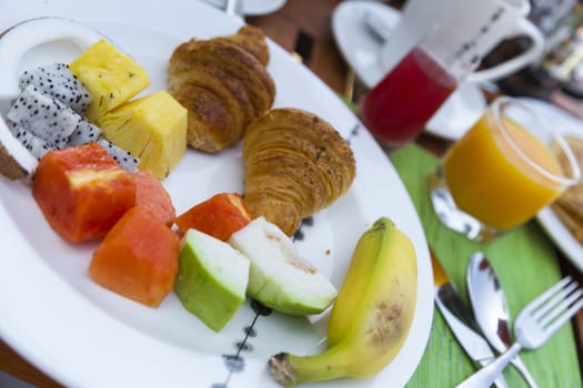 Delicious healthy breaklfast outdoors in a wooden table with sea at background. The breakfast consists of fresh fruit and waffles with pancakes.