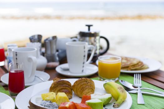 Delicious healthy breaklfast outdoors in a wooden table with sea at background. The breakfast consists of fresh fruit and waffles with pancakes.