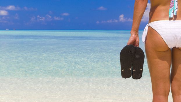 Woman holding flip flops while standing on the beach.