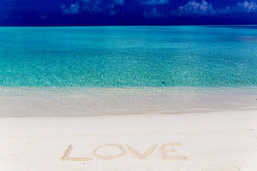 Word love written on sand in Maldives with the lagoon at background.