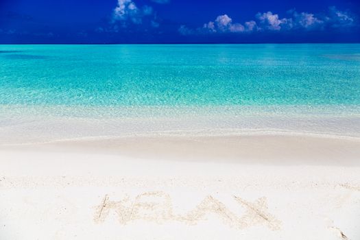 Word relax written on sand in Maldives with the lagoon at background.