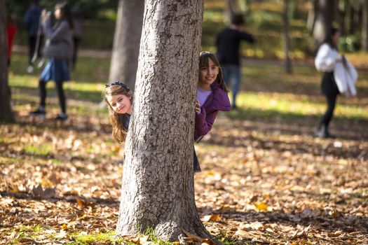 Two friends having fun hiding behind a tree.