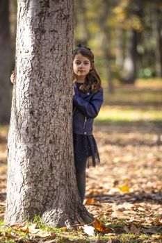 Little girl in the park leaning in a tree.