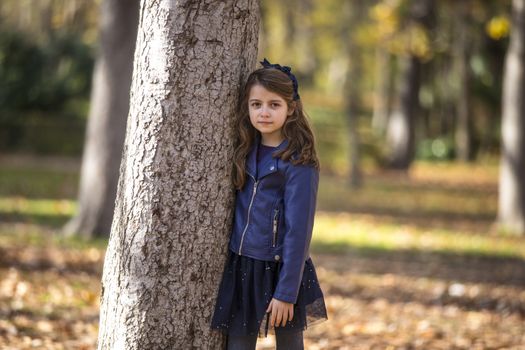 Little girl in the park leaning in a tree.