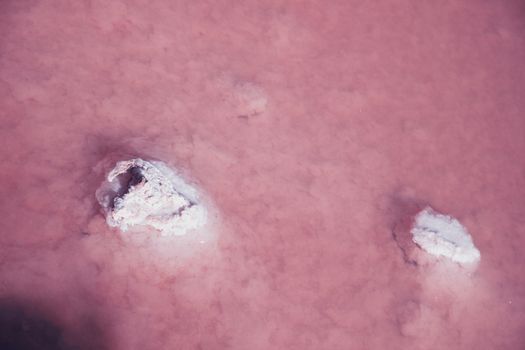 Textured of different shapes of rocks of salt in a pink water basin.