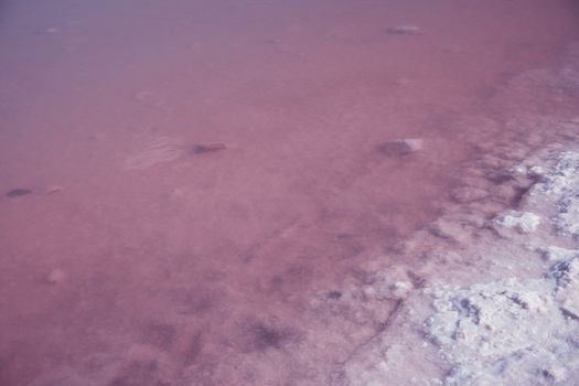 Textured of different shapes of rocks of salt in a pink water basin.