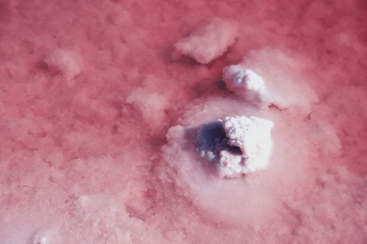 Textured of different shapes of rocks of salt in a pink water basin.