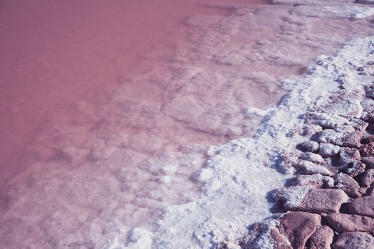 Textured of different shapes of rocks of salt in a pink water basin.