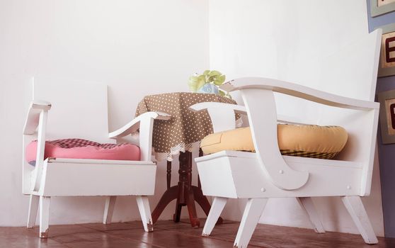 White wooden chairs and wooden table with beautiful color table covers and cute small flower vase in the living corner at the cafe. Relaxation corner decoration idea.