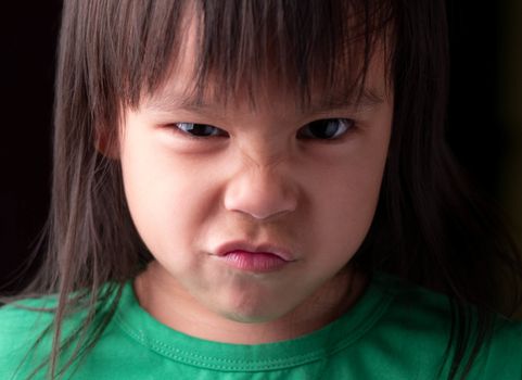 Portrait face of Asian little child girl with angry expression on dark background.