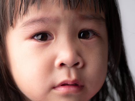 Portrait face of Asian little child girl with sad expression on dark background.