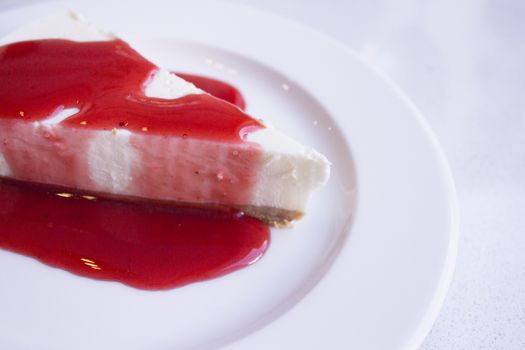White plate with cheese cake with strawberry syrup