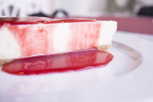 White plate with cheese cake with strawberry syrup