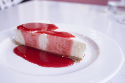 White plate with cheese cake with strawberry syrup