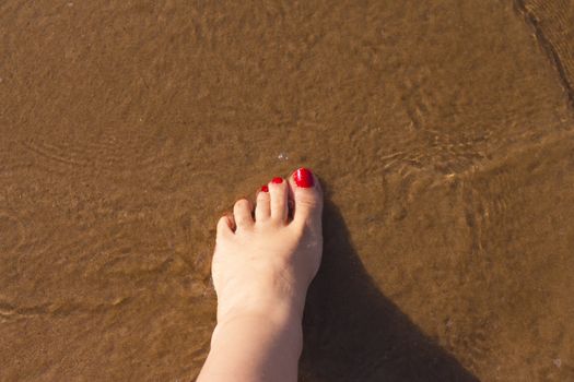 Beach scene with woman feet on the sand. Nails of feet painted red