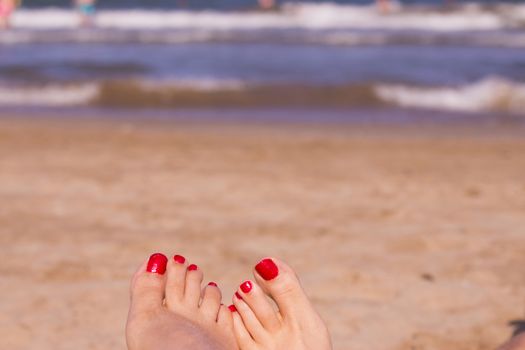 Beach scene with woman feet on the sand. Nails of feet painted red