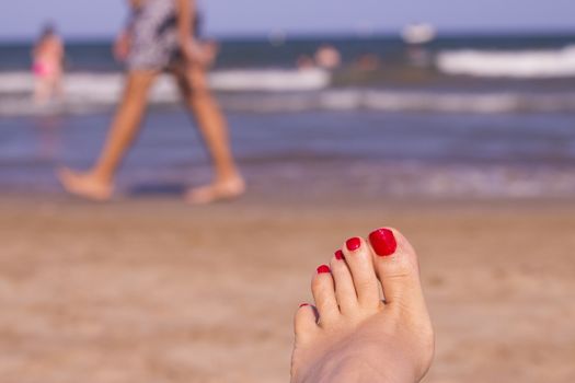 Beach scene with woman feet on the sand. Nails of feet painted red