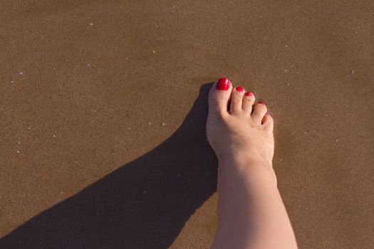 Beach scene with woman feet on the sand. Nails of feet painted red