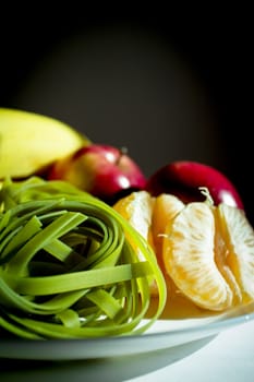 Plate with bananas, apples, tangerine and spinach pasta without cooking