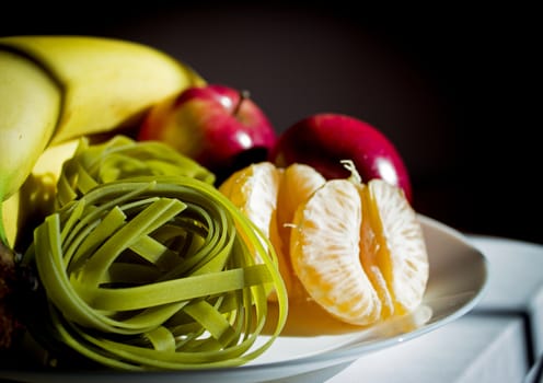 Plate with bananas, apples, tangerine and spinach pasta without cooking
