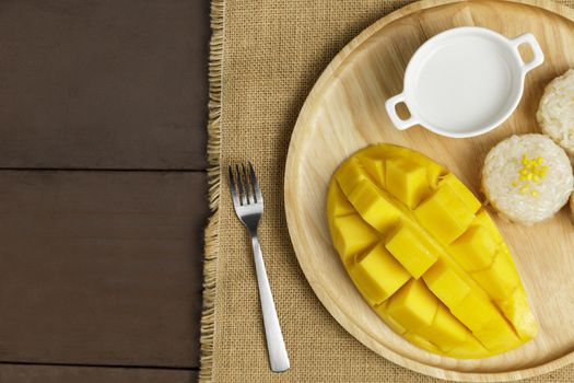 Top view Yellow half  mango with small fork. Mango fruit cubes on the wooden table. Tropical fruit asia. Fresh yellow mango peel and Sliced cubes on wood butcher. Dessert fruit.