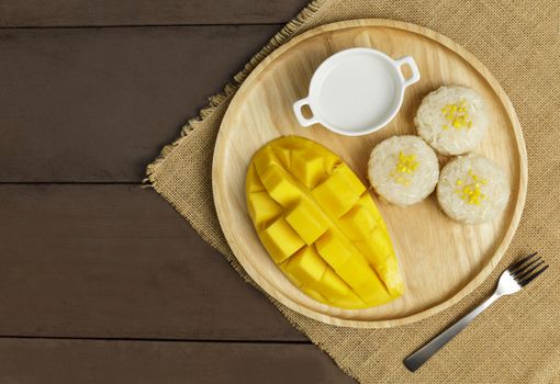 Top view Yellow half  mango with small fork. Mango fruit cubes on the wooden table. Tropical fruit asia. Fresh yellow mango peel and Sliced cubes on wood butcher. Dessert fruit.