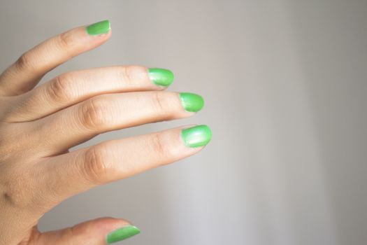 Woman hand isolated on neutral background with nails painted bright green