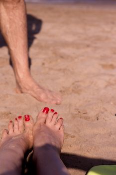 Beach scene with woman feet on the sand. Nails of feet painted red