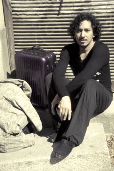 Man sitting on the floor tired with his luggage beside. Urban background