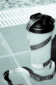 Shake mix bottle surrounded by a measuring tape on the edge of a summer pool