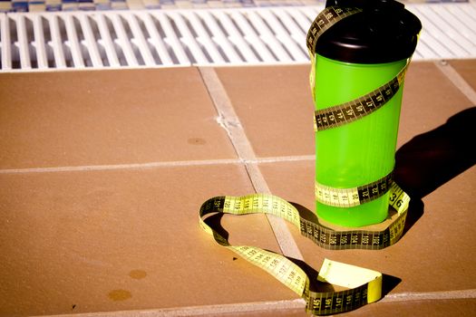 Shake mix bottle surrounded by a measuring tape on the edge of a summer pool