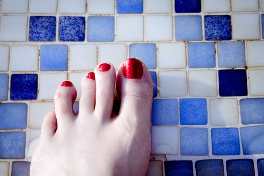 Bare feet of woman with nails painted red. Pool background