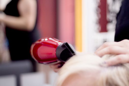Hairdresser drying hair with red hand dryer