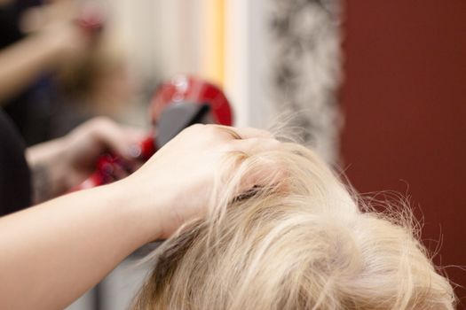 Hairdresser drying hair with red hand dryer