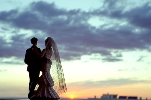 Silhouette of newlyweds with sunrise background. Romantic scene. Figures of the bridal cake, they are not real people