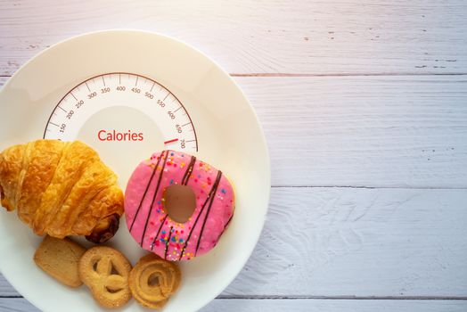 Calories counting and food control concept. doughnut ,croissant and cookies on white plate with tongue scales for Calories measuring