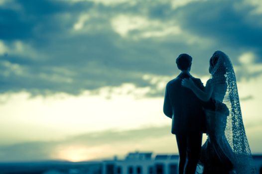 Silhouette of newlyweds with sunrise background. Romantic scene. Figures of the bridal cake, they are not real people