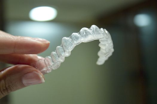 Womans hand holding transparent dental orthodontics to correct the dental alignment. Dark background