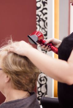 Hairdresser drying hair with red hand dryer