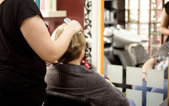 Hairdresser in positive attitude brushing the hair of a client