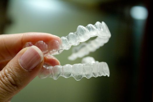 Womans hand holding transparent dental orthodontics to correct the dental alignment. Dark background