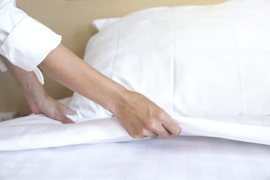 Close up hand set up white bed sheet in hotel room