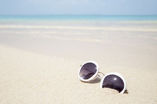 Sunglasses on sandy beach of blue sea in summer