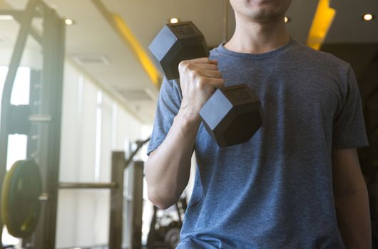 Young man beginner exercising with dumbbell flexing muscles at gym, sport training concept